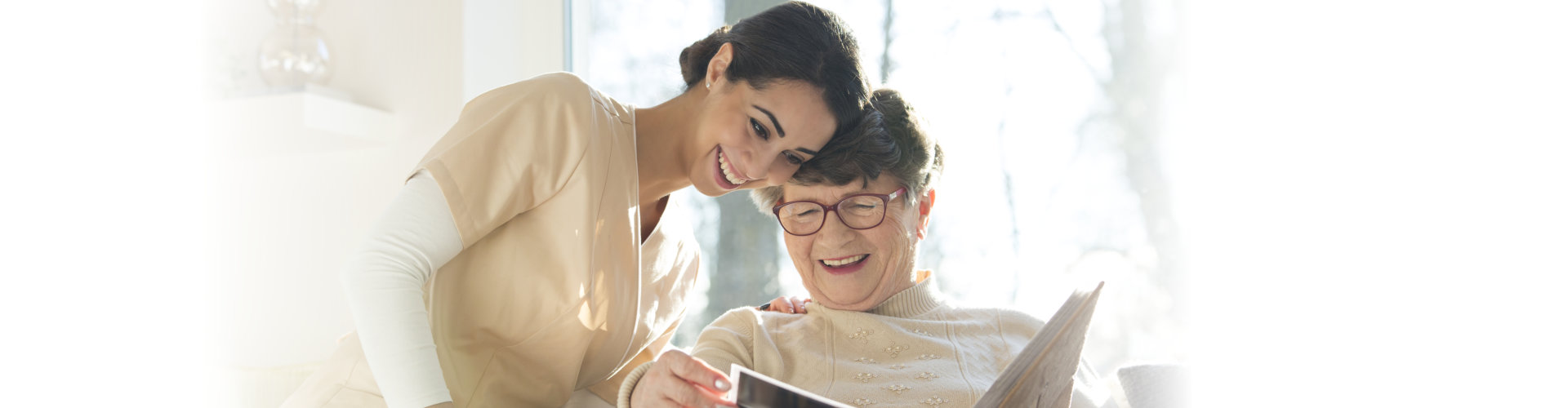 Smiling senior women watching photo album with happy caregiver